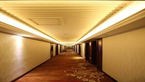 Corredor longo e estreito de hotel, com carpete estampado e teto com iluminação embutida.