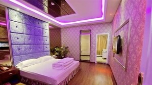 Quarto moderno com cama grande, TV fixada na parede e iluminação roxa no teto.