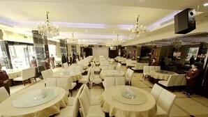 Um restaurante espaçoso com mesas redondas e cadeiras brancas, lustres e um design de interiores moderno.