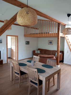 Een eetruimte met een houten tafel en stoelen, een trap en een vide met een houten balustrade.