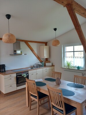 Een keuken met houten balken, een eettafel met stoelen en hanglampen.