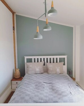 Un dormitorio con una cama blanca, dos mesitas de noche y una pared verde.