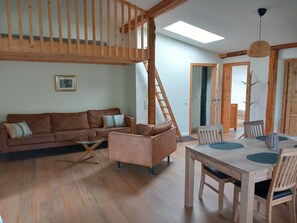 Een ruime woonkamer met een houten trap, een zithoek, een eettafel met stoelen en een dakraam.