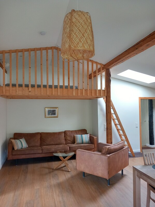Un espacio habitable estilo loft con una escalera de madera, un juego de sofás, una mesa de centro y una mesa de comedor.
