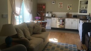 A living room with a sofa, a dining table, and a kitchen area with cabinets and appliances. - The Dog house, a country retreat. (Bodorgan)