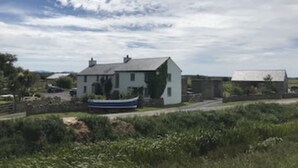 A white house with a grey roof, surrounded by greenery and a boat in the background. - The Dog house, a country retreat. (Bodorgan)