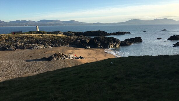 A coastal landscape with a lighthouse, rocky terrain, and a sandy beach. - The Dog house, a country retreat. (Bodorgan)