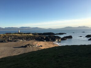 Un paisaje costero con un faro, terreno rocoso y una playa de arena.