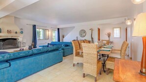 A spacious living area with a blue sofa set, a dining table with wicker chairs, and a fireplace. - Reves de Rives by Interhome (Agay Saint Raphael)