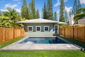 Une maison avec une piscine, entourée d’une clôture en bois et de grands arbres.