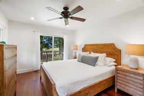 Une chambre à coucher avec un lit en bois, deux tables de chevet avec des lampes, un ventilateur de plafond et une vue sur la verdure par une fenêtre.