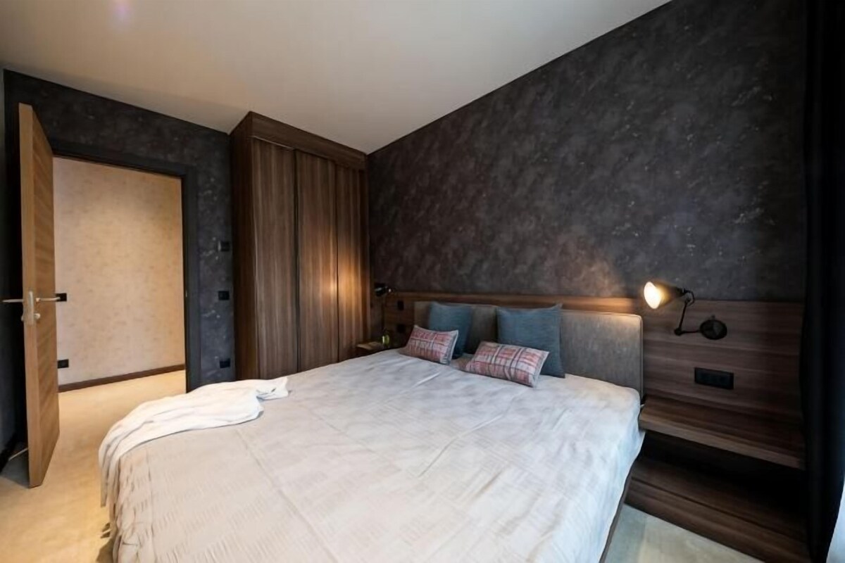 Quarto com uma cama grande, um guarda-roupa e cabeceira com iluminação embutida.