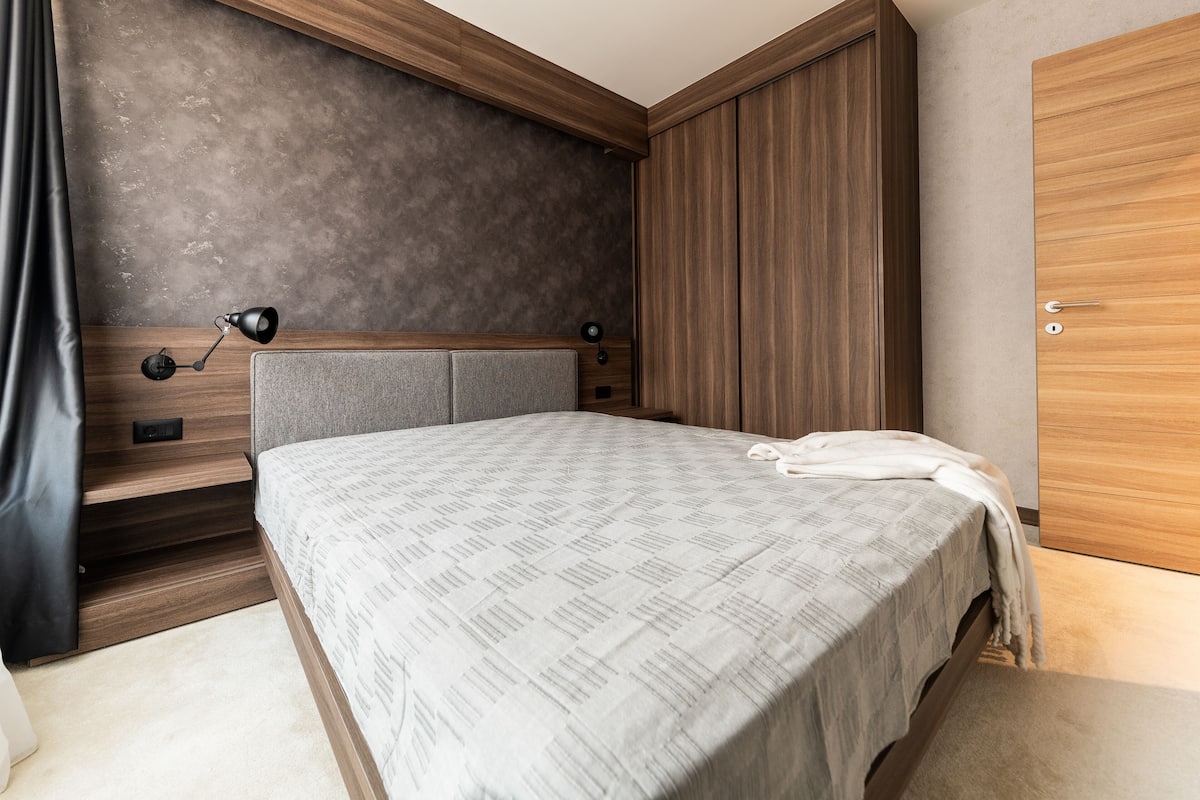 A bedroom with a bed, bedside table, lamp, and wardrobe.