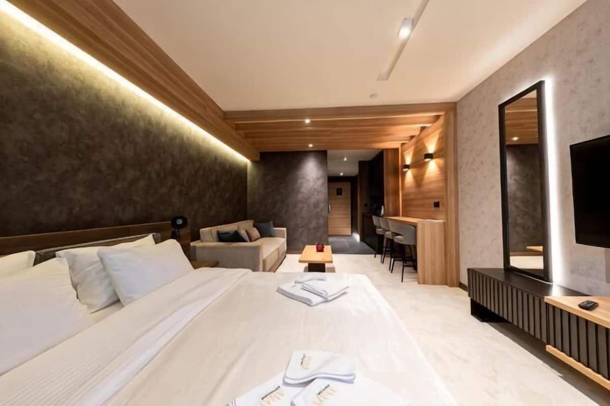 A modern hotel room with a large bed, a desk, a sofa, and a TV.