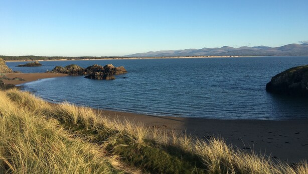 A coastal landscape with a clear sky, calm sea, and distant mountains. - Duck House  (Bodorgan)