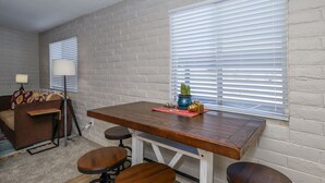 Ein Essbereich mit Holztisch und Barhocker, einer Ziegelwand und einem Fenster mit Jalousien.