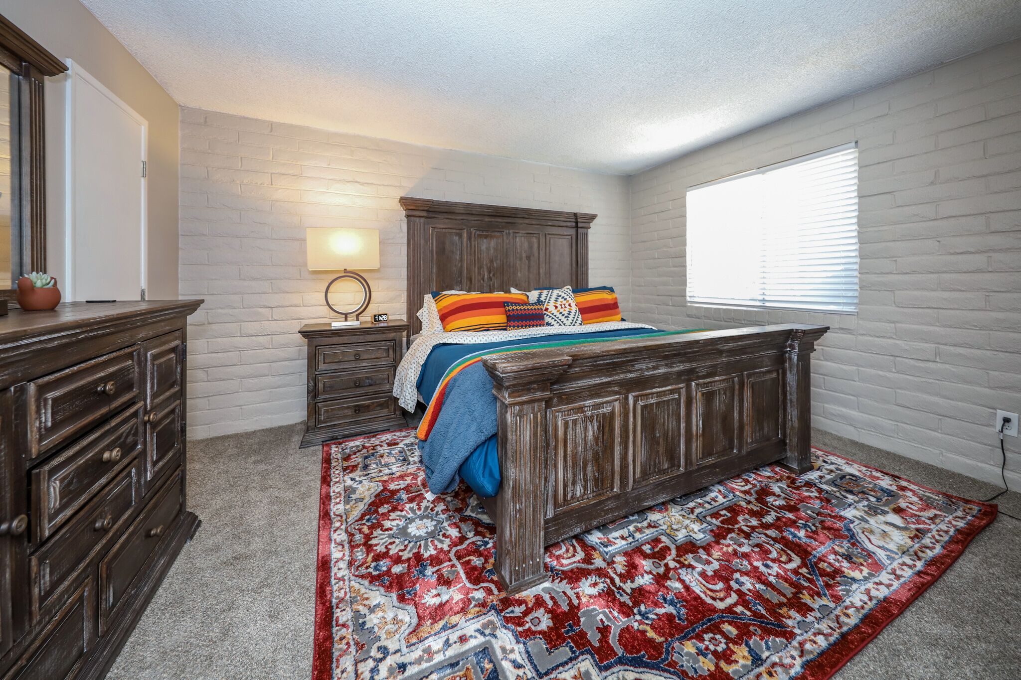 Un dormitorio con una cama de madera, una mesita de noche, un aparador, una lámpara y una ventana con persianas.