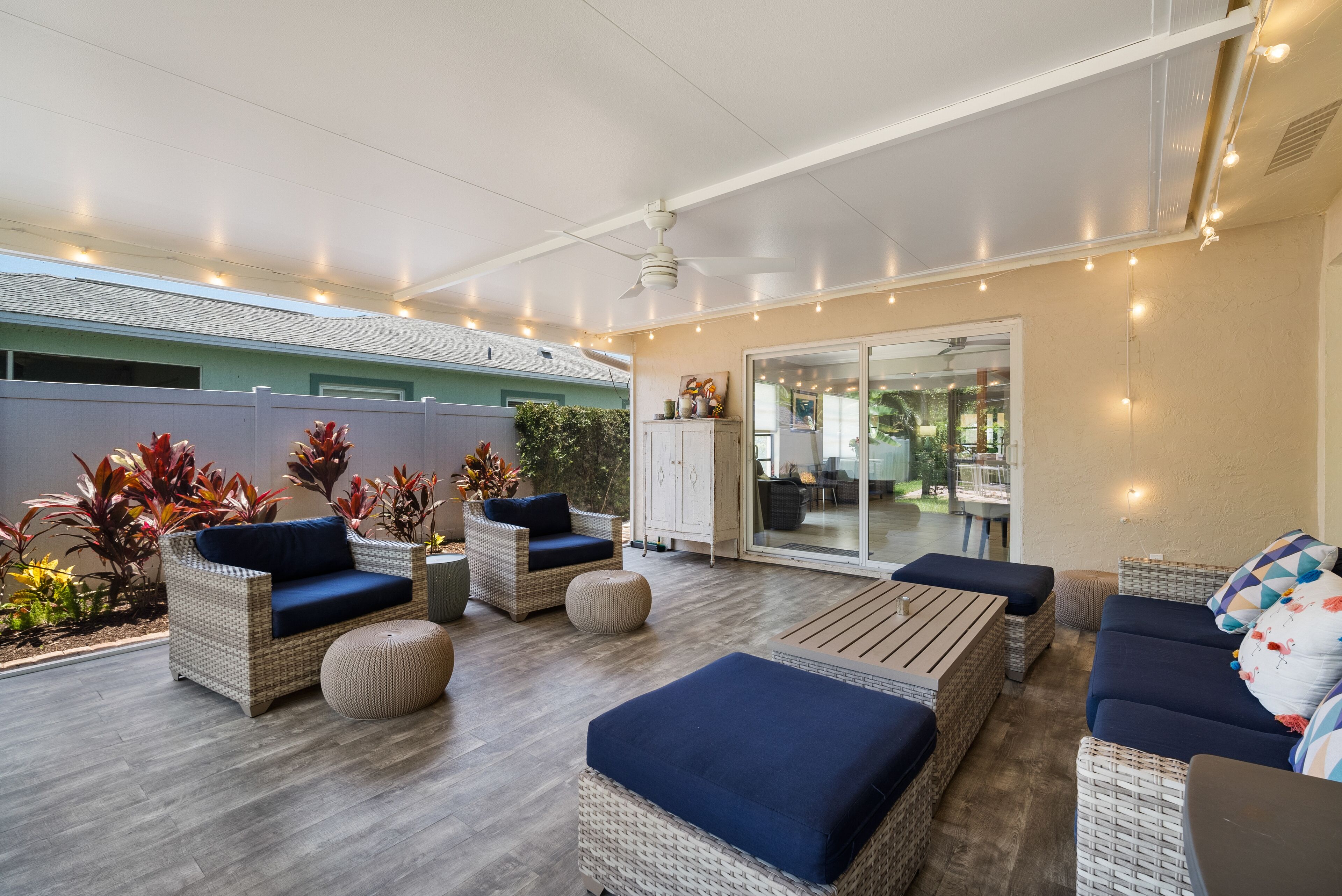 Une terrasse extérieure avec des meubles en osier, un ventilateur de plafond et des guirlandes lumineuses.