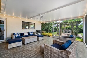 A covered outdoor seating area with wicker furniture and cushions, a ceiling fan, and a view of greenery outside. - Walk to the beach, restaurants, grocery and more! Enjoy all Naples has to offer (Naples)