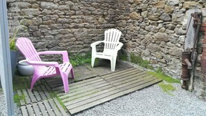 Een stenen muur met twee Adirondack-stoelen, één roze en één wit, op een houten terras.