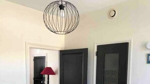Een gang met een zwarte deur, een rode lamp en een hanglamp.