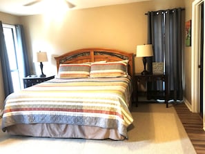 A neatly made bed with a striped bedspread and two pillows, a bedside table with a lamp, and a framed sign on the wall.