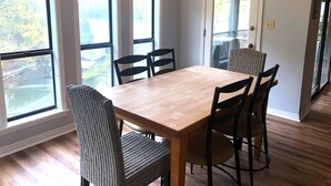 A dining area with a wooden table and wicker chairs, large windows with blinds, and a chandelier. - 4 bedroom lake house at Pickwick (Counce)