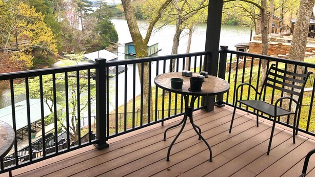 A covered outdoor area with a wooden deck, a round table with chairs, and a view of a lake and trees. - 4 bedroom lake house at Pickwick (Counce)