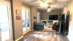 A spacious living area with hardwood flooring, a ceiling fan, a television, and a sliding glass door leading to a balcony. - 4 bedroom lake house at Pickwick (Counce)