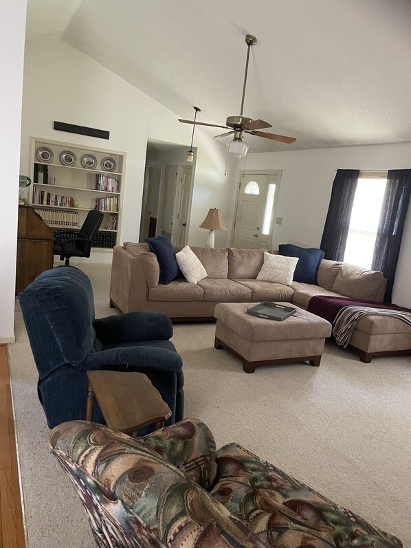 A living room with a sectional sofa, a blue armchair, a patterned couch, and a ceiling fan.