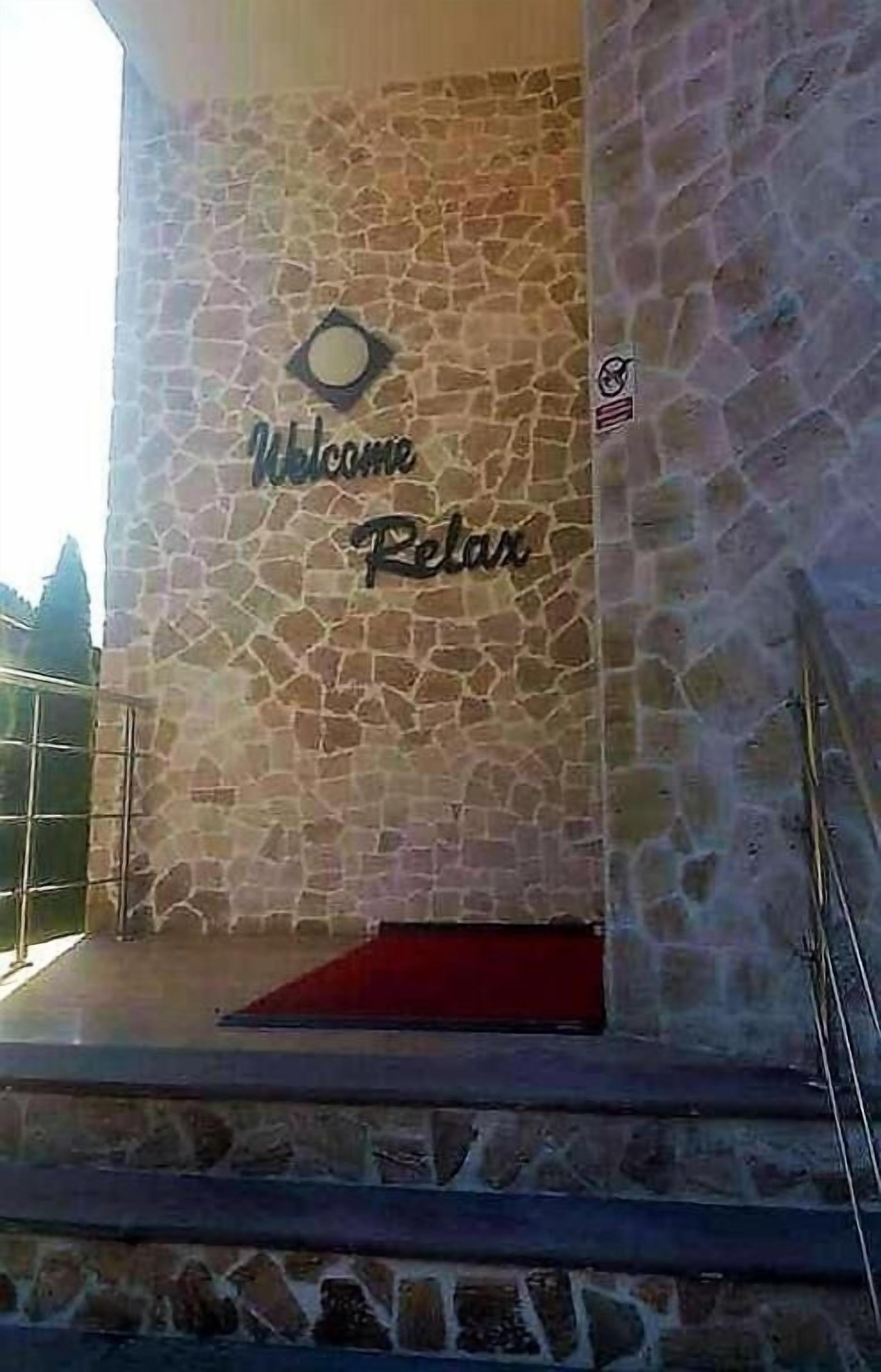 Un muro de piedra con un letrero que dice "Welcome Relax" y una alfombra roja que lleva a una escalera.