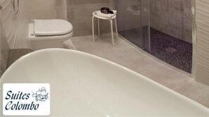 A modern bathroom with a bathtub, toilet, and a glass-enclosed shower area. - Suites Colombo (La Spezia)