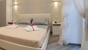 A modern bedroom with a large bed, two bedside tables, and a decorative wall. - Suites Colombo (La Spezia)