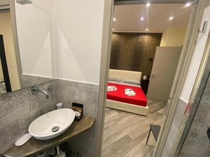 A modern bathroom with a large sink and a bed with a red bedspread. - Suites Colombo (La Spezia)