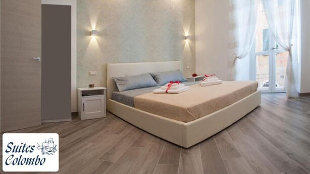 A modern bedroom with a large bed, bedside tables, and a view of the outside. - Suites Colombo (La Spezia)