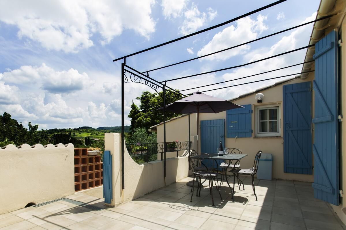 Une terrasse avec une table et des chaises, un parasol bleu et une vue sur la campagne.