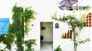 Un edificio blanco con puerta azul, una entrada pequeña y plantas en macetas.