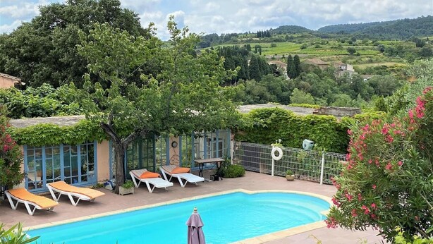 Una piscina con sillas de descanso y una pérgola, rodeada de exuberante vegetación y colinas al fondo.