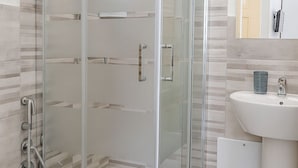 Un baño moderno con ducha de vidrio, un lavamanos blanco y un felpudo a rayas.