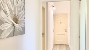 Un pasillo con suelo de madera, una puerta blanca con un número y un cuadro grande de una flor blanca en la pared.