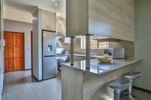 A modern kitchen with a central island, stainless steel appliances, and a wooden door. - Howard Davis 28B by CTHA (Cape Town)