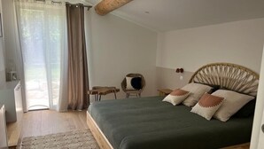 A bedroom with a wooden bed frame, a green bedspread, and a woven rug. There is a window with curtains, a chair, and a small table. - Charming and elegant villa (Tarascon)