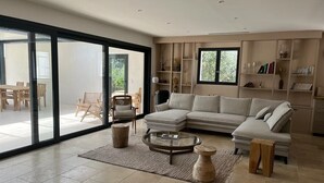 A modern living room with a sectional sofa, a glass coffee table, and a large sliding glass door leading to an outdoor area. - Charming and elegant villa (Tarascon)