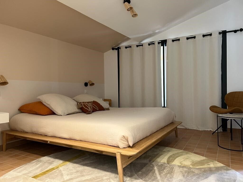 Een slaapkamer met een houten bed, wit beddengoed, een klein tafeltje en een stoel.