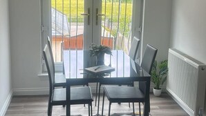 A dining area with a table and chairs, a potted plant, and a view of a garden through a glass door. - Cozy Lanarkshire Apartment With a View (Larkhall)