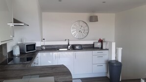 A modern kitchen with white cabinets, stainless steel appliances, and a large wall clock. - Cozy Lanarkshire Apartment With a View (Larkhall)
