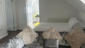 A bedroom with a sloped ceiling, a bed with white bedding, and a window with a view of a garden. - Cozy Lanarkshire Apartment With a View (Larkhall)