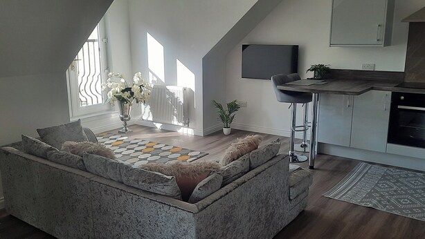 A modern loft with a stone seating area, a kitchen with a built-in oven, and a large window providing natural light. - Cozy Lanarkshire Apartment With a View (Larkhall)