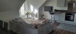 A modern loft with a stone seating area, a kitchen with a built-in oven, and a large window providing natural light. - Cozy Lanarkshire Apartment With a View (Larkhall)