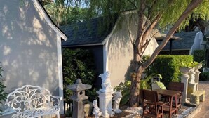 A patio area with a white bench, a table with chairs, decorative statues, and a pergola structure.